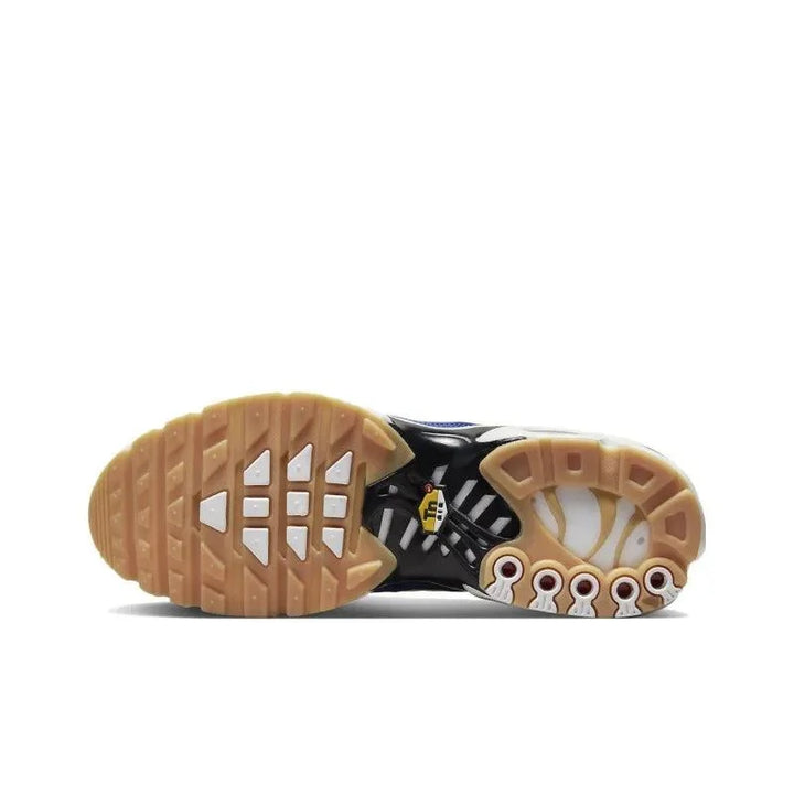 Sole view of a black and white athletic sneaker with a tan rubber outsole.